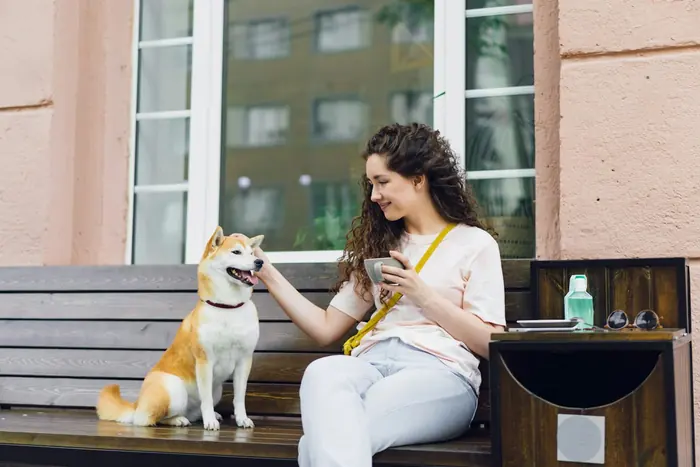 A woman on a bench with her dog, smiling at her phone